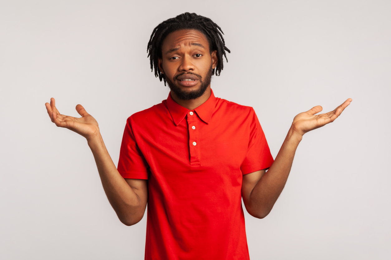 Handsome bearded man with dreadlocks wearing red casual style T-shirt, standing with raised arms and looking at camera with answer. Indoor studio shot isolated on gray background.