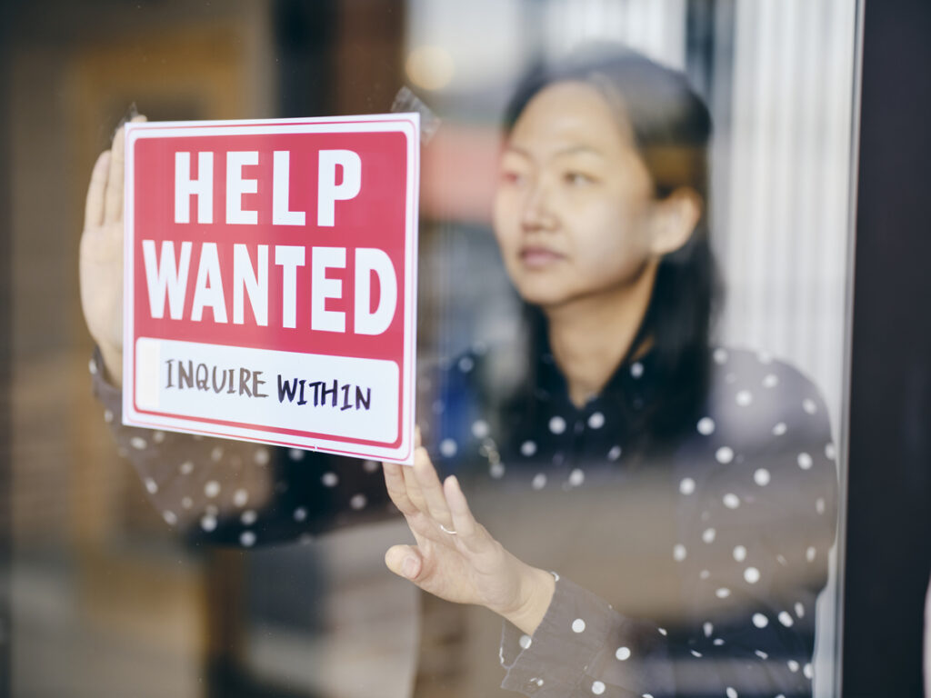 A small business owner, putting up a help wanted sign in her store window.