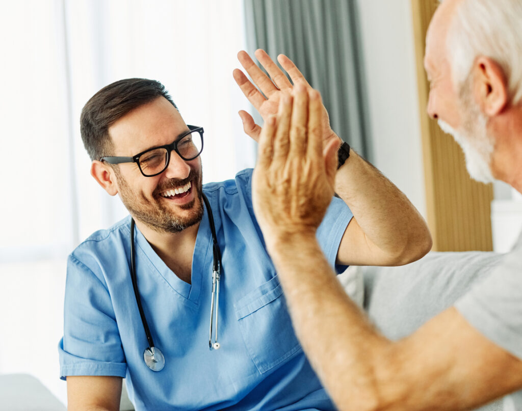 Doctor or nurse home health caregiver with senior man giving high five at home or nursing home